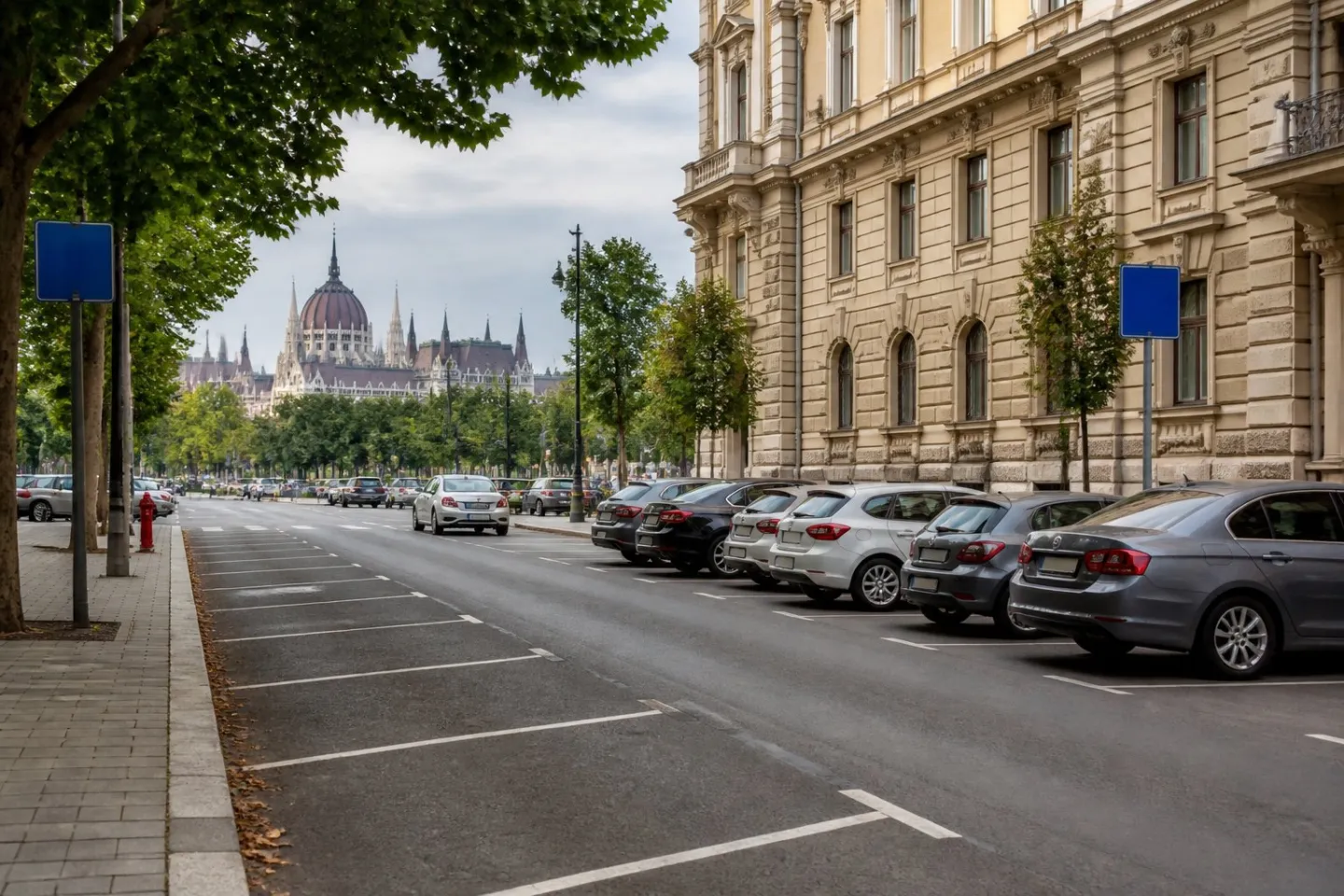Parked cars line an urban street in Budapest with historic buildings in the background.